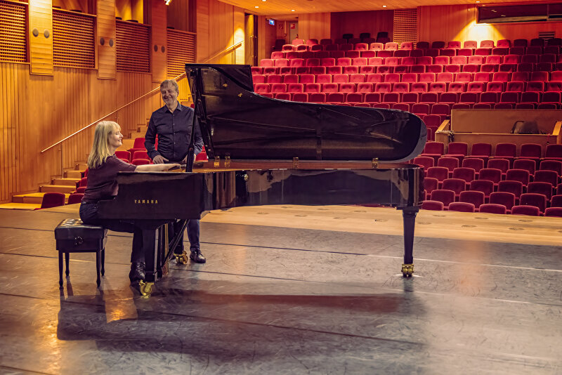Joachim en Rani van Pianoservice Den Haag poseren trots bij een concertvleugel in Theater Schiedam, een theaterzaal met 800 zitplaatsen, waaraan zij onlangs onderhoud hebben gepleegd.
